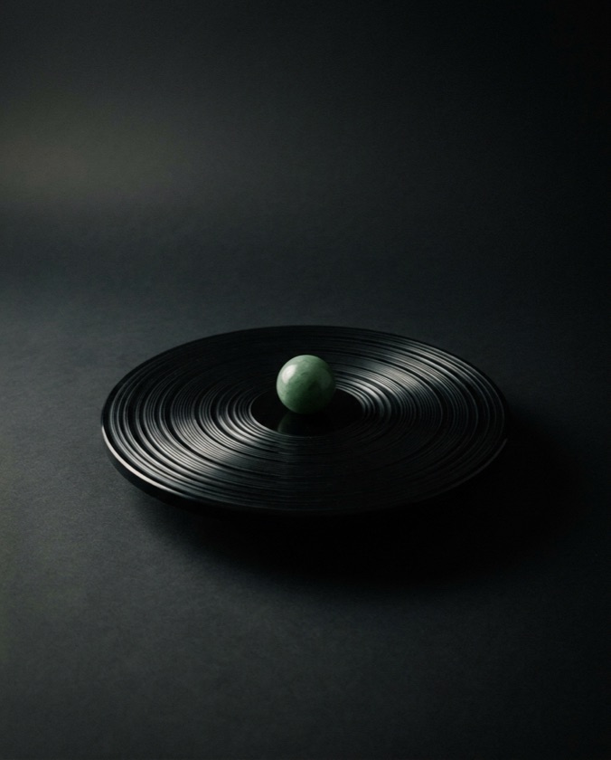 Abstract still-life sculpture: a jade-green sphere held at the center of concentric obsidian rings — a quiet emblem of Alfred's watch